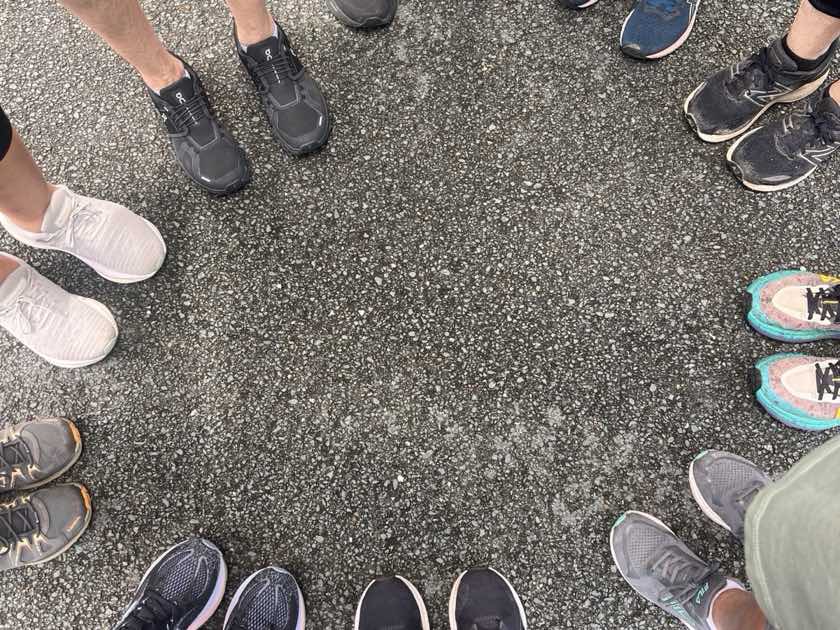 Twelve pairs of walking shoes arranged in a wide circle on tarmac, the women standing in them out of frame &mdash; the Noosa Walk and Talk group before setting off.